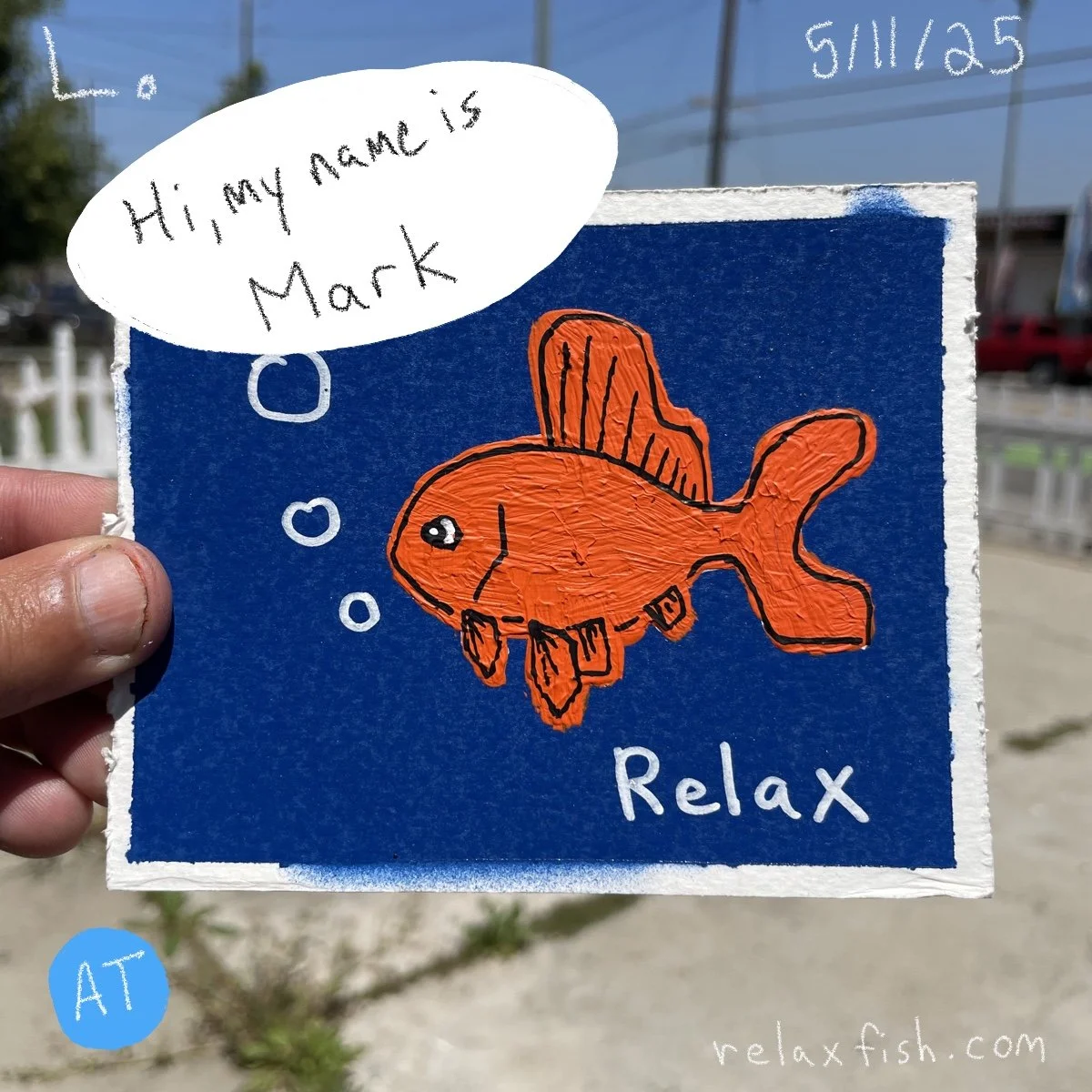A hand holding a blue card with an orange drawing of a fish that has a speech bubble saying, 'Hi, my name is Mark.' The card has the words 'Relax' and 'O' with bubbles, and the website relaxfish.com is written at the bottom.