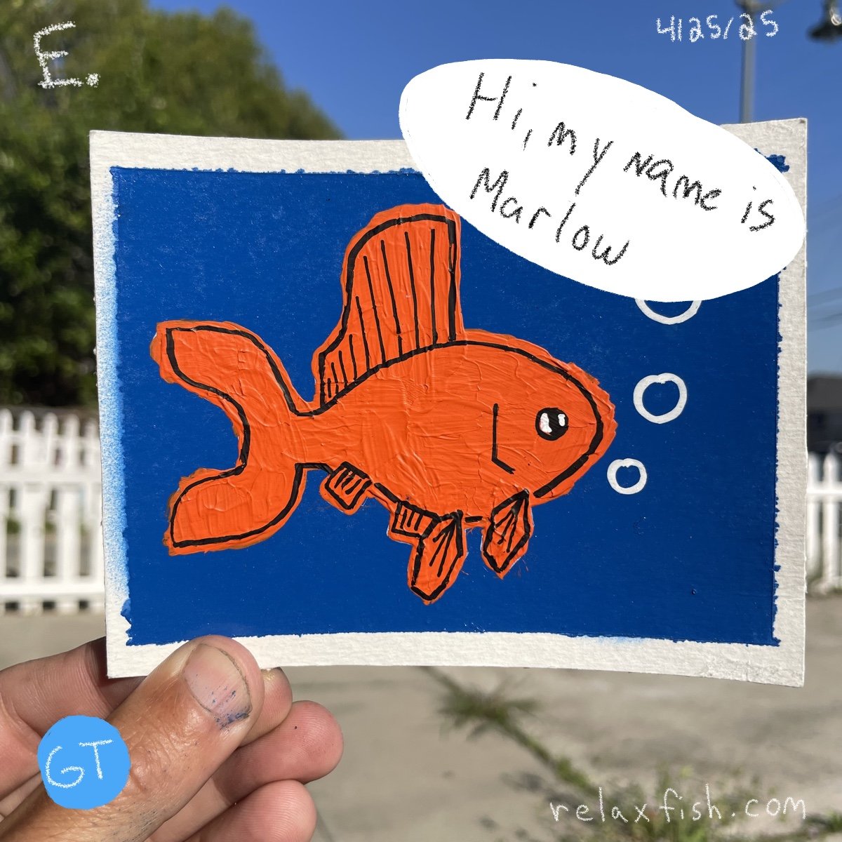 Handmade drawing of an orange fish with a large fin on a blue background. A speech bubble says, 'Hi, my name is Marlow.' The image has a website URL, relaxfish.com, at the bottom right. The hand holding the drawing is visible.