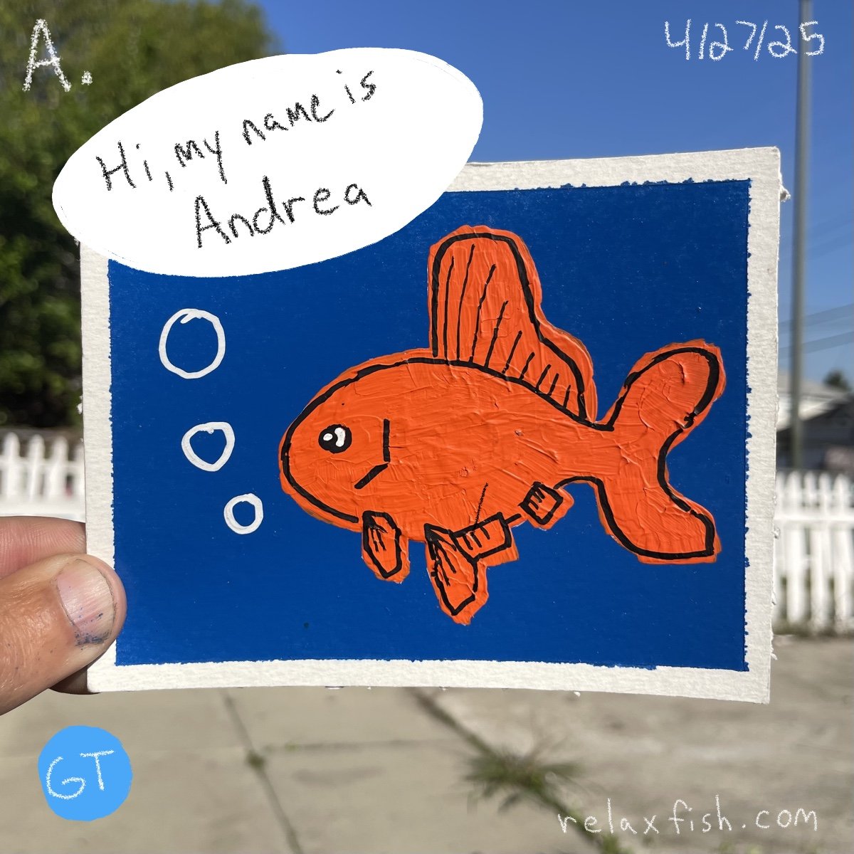 A hand-held drawing of an orange fish with a side fin and a tail fin, set against a blue background, with a speech bubble saying, "Hi, my name is Andrea." The drawing includes three white bubbles, and the date 4/27/25 is written in the top right corn