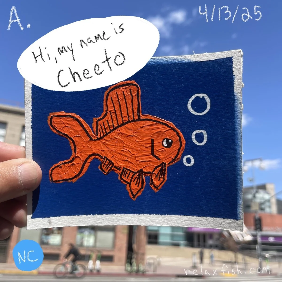 A hand holding a blue card with a drawing of a red fish wearing a top hat. A speech bubble says, 'Hi, my name is Cheto.' The date 4/13/25 is in the top right corner.