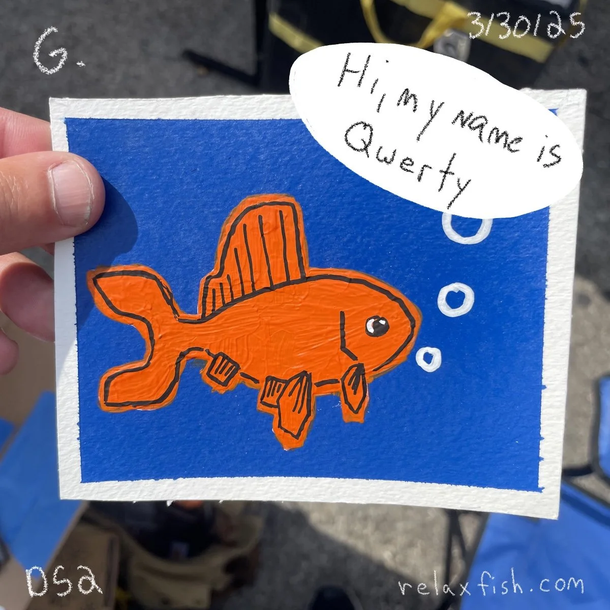 A colorful drawing of an orange fish wearing a brown hat and sitting underwater, with bubbles rising from its mouth. There is a speech bubble with the message, "Hi, my name is Qwerty." The background is blue, and the drawing is on a piece of textured