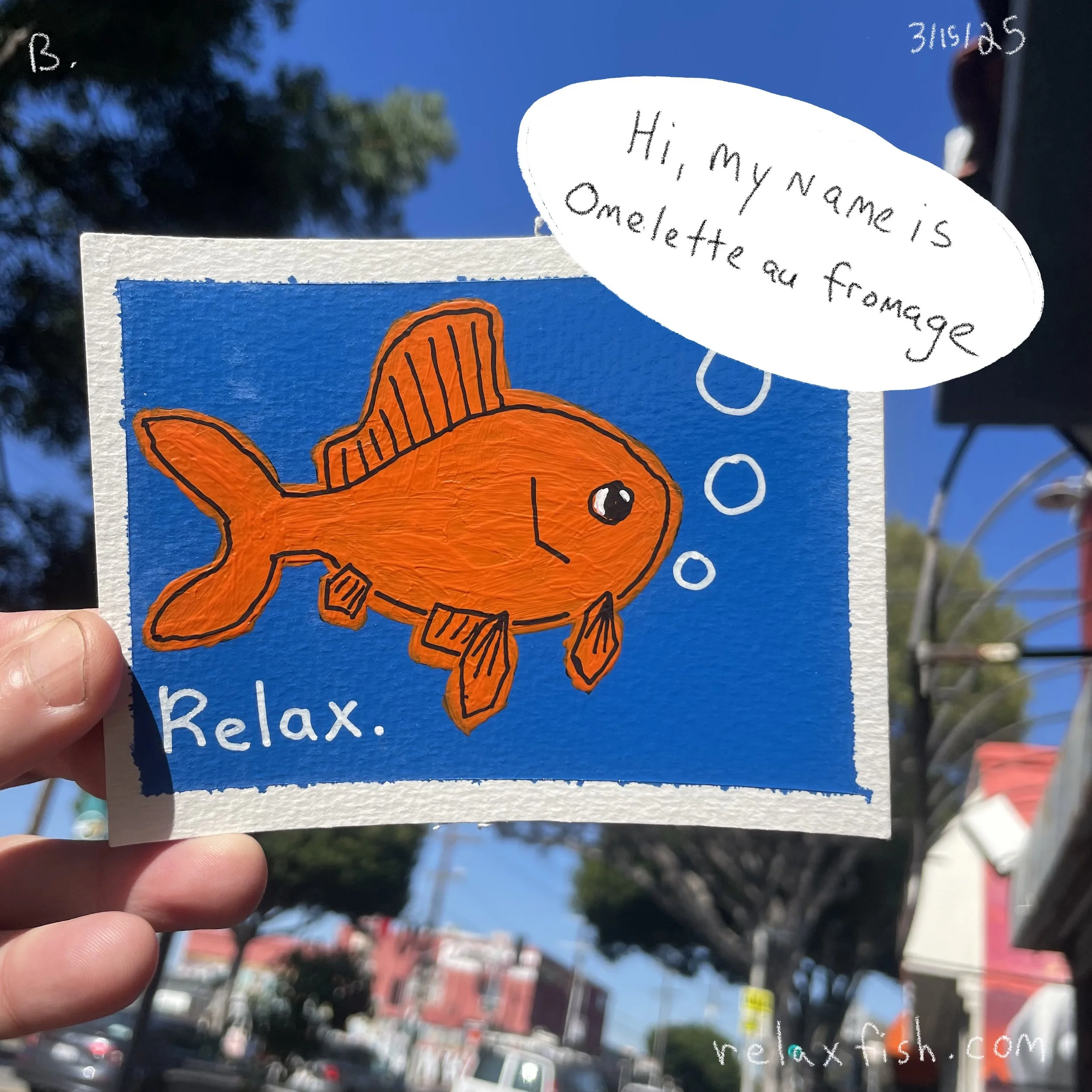 Hand holding a colorful drawing of an orange fish with the word "Relax" written below. The drawing includes a speech bubble that says, "Hi, my name is Omelette au frommage." The background of the drawing is blue, and the photo is taken outdoors with 