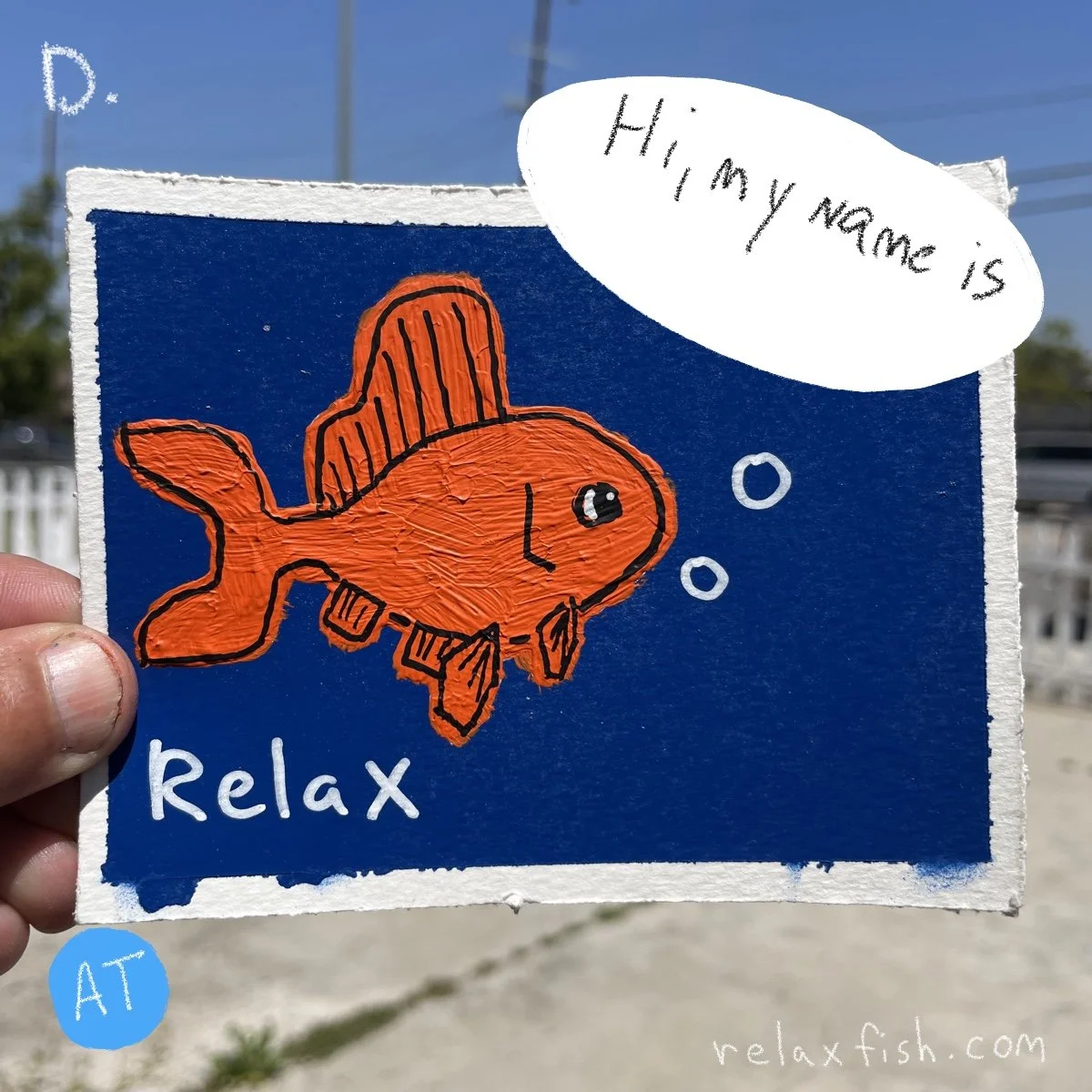 A hand holding a drawing of a cartoon orange fish wearing a hat, with the words "Relax" and "Hi, my name is" in a speech bubble. The background is blue with white bubbles and the website relaxfish.com.