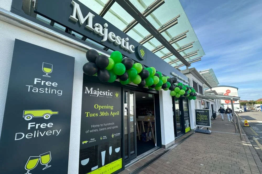 The exterior of Majestic Wines store decorated with black and green balloons, announcing its opening on April 30th. Signs indicate free tasting, free delivery, and a now open status.
