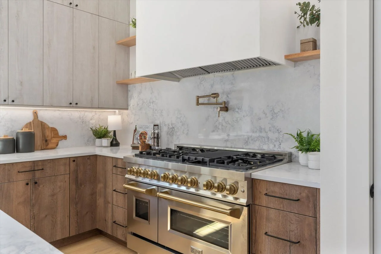 Modern kitchen with stainless steel oven and gas stove, wooden cabinets, white countertops, and decor including plants, a lamp, and kitchen accessories.