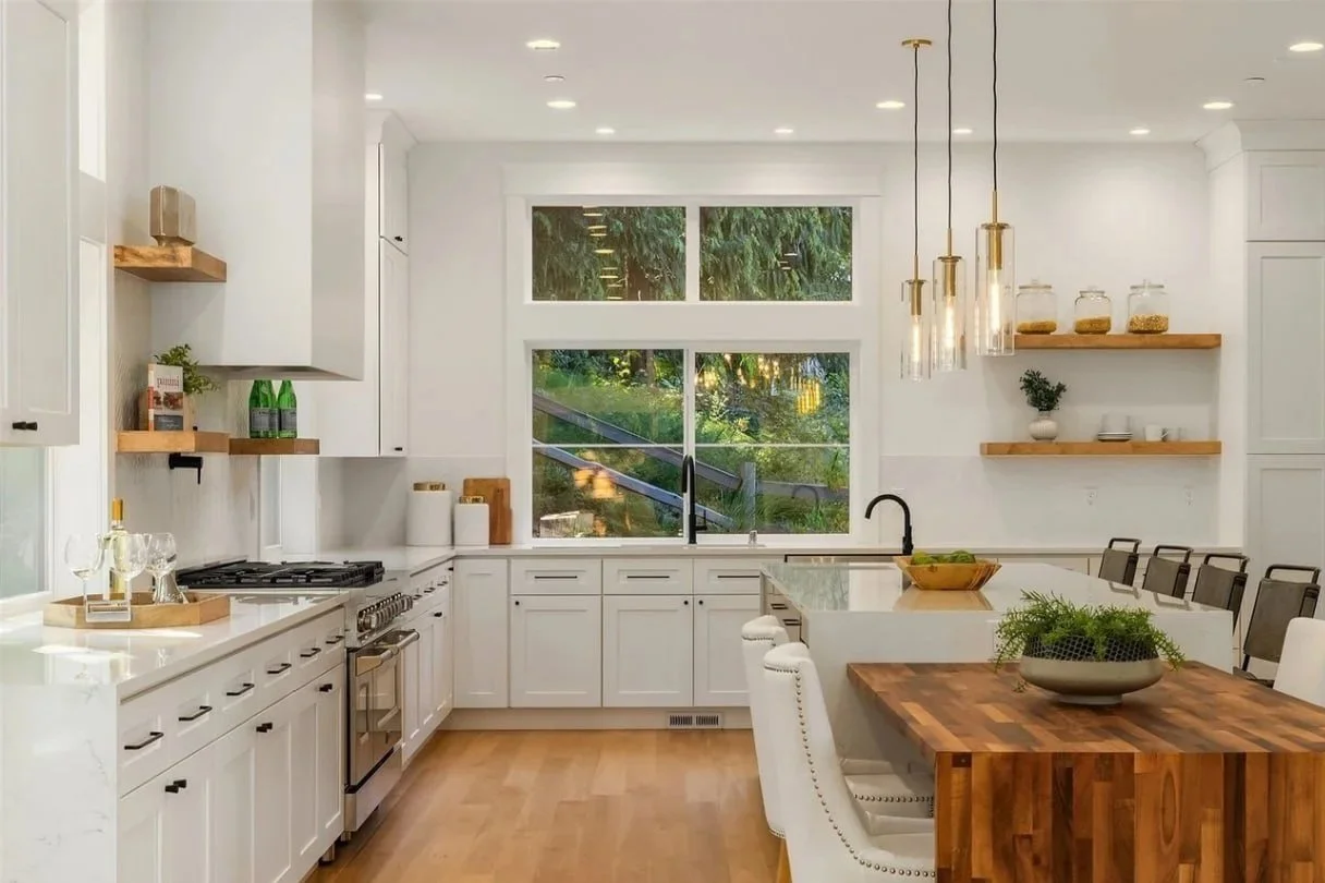 Modern white kitchen with wooden accents, large window, and a kitchen island with seating.