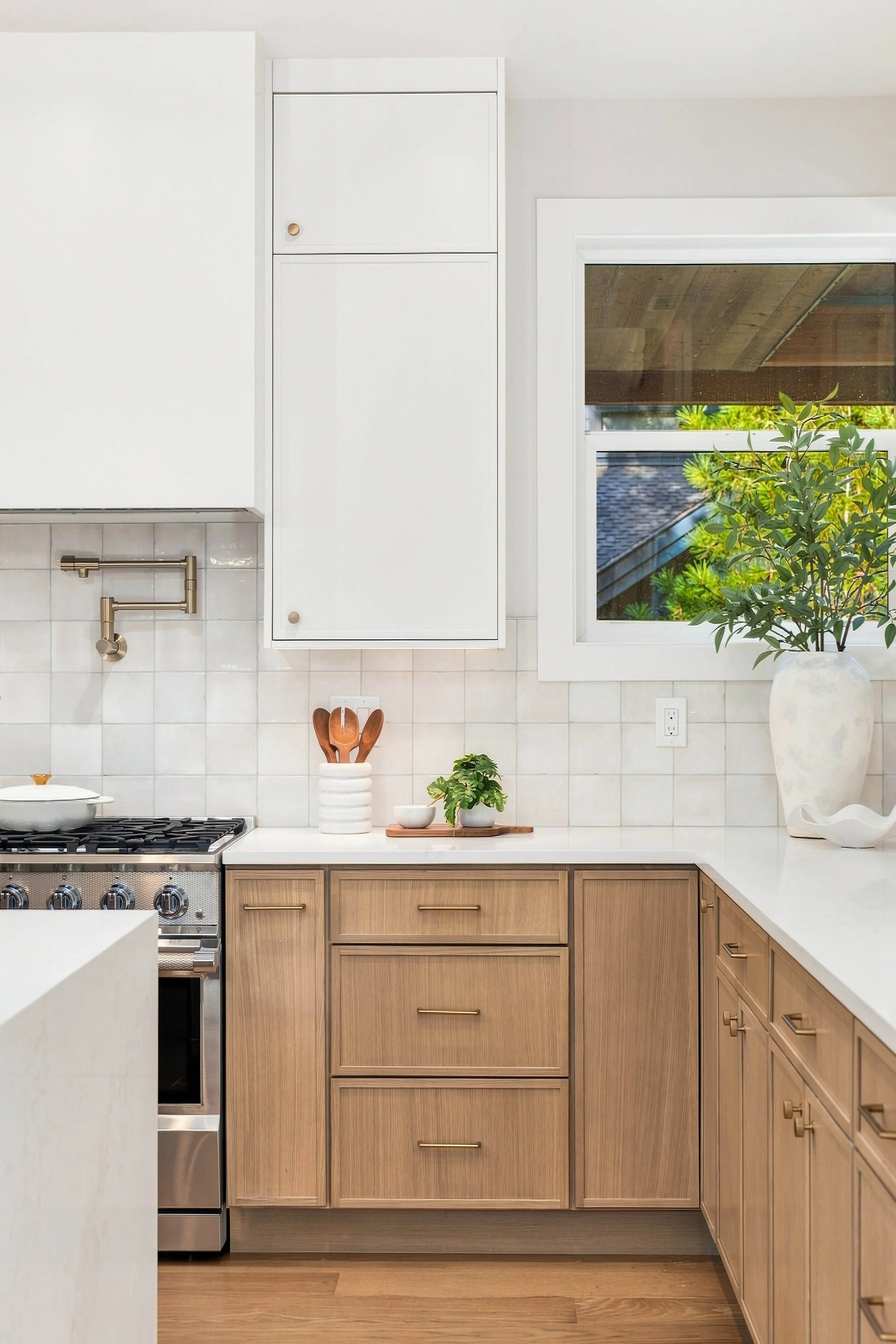 Kitchen with wooden cabinets, white countertops, a stove, a window with a view of greenery, and a potted plant on the counter.