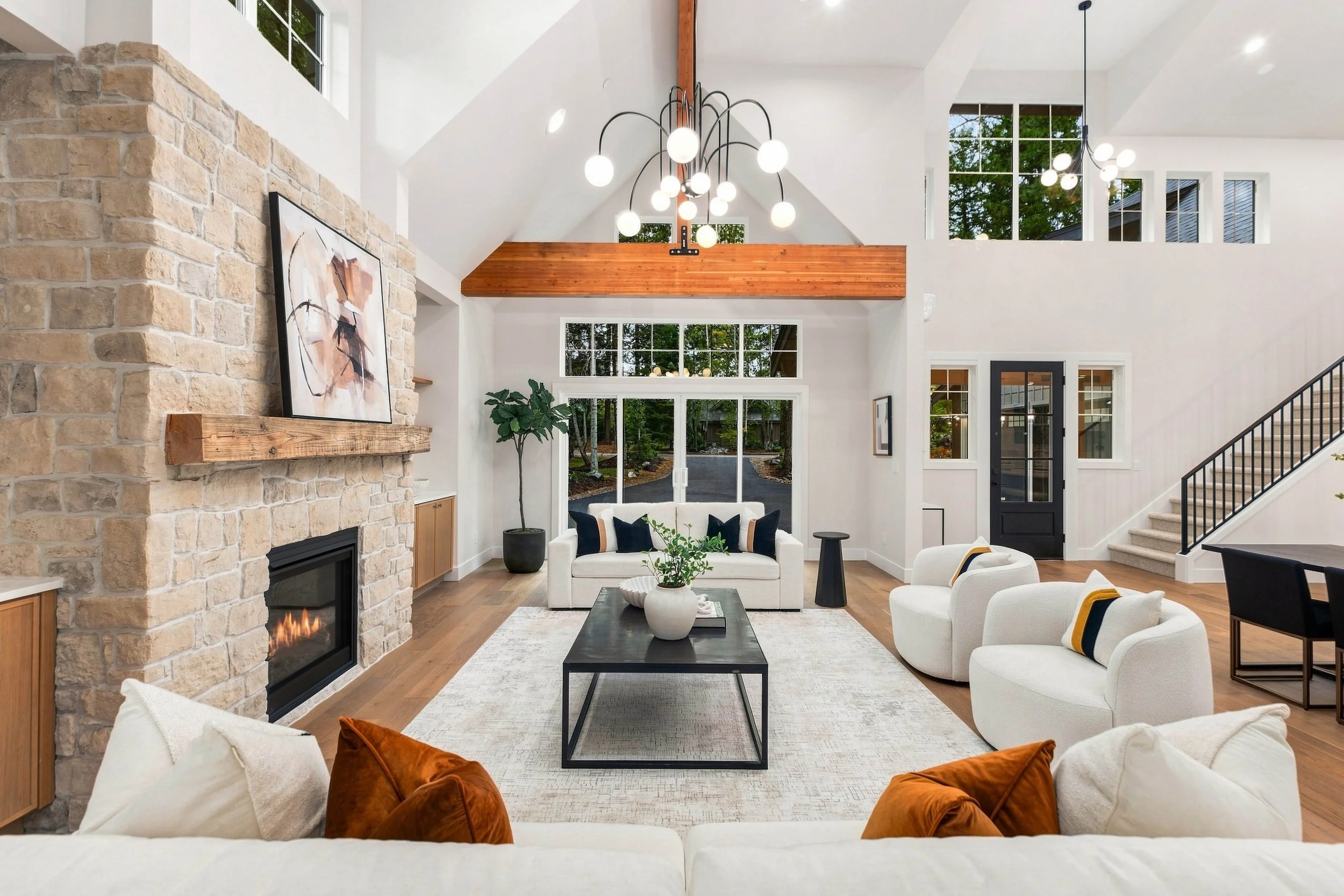 Interior of a spacious, modern living room with high ceilings, large windows, a stone fireplace, and contemporary furniture.