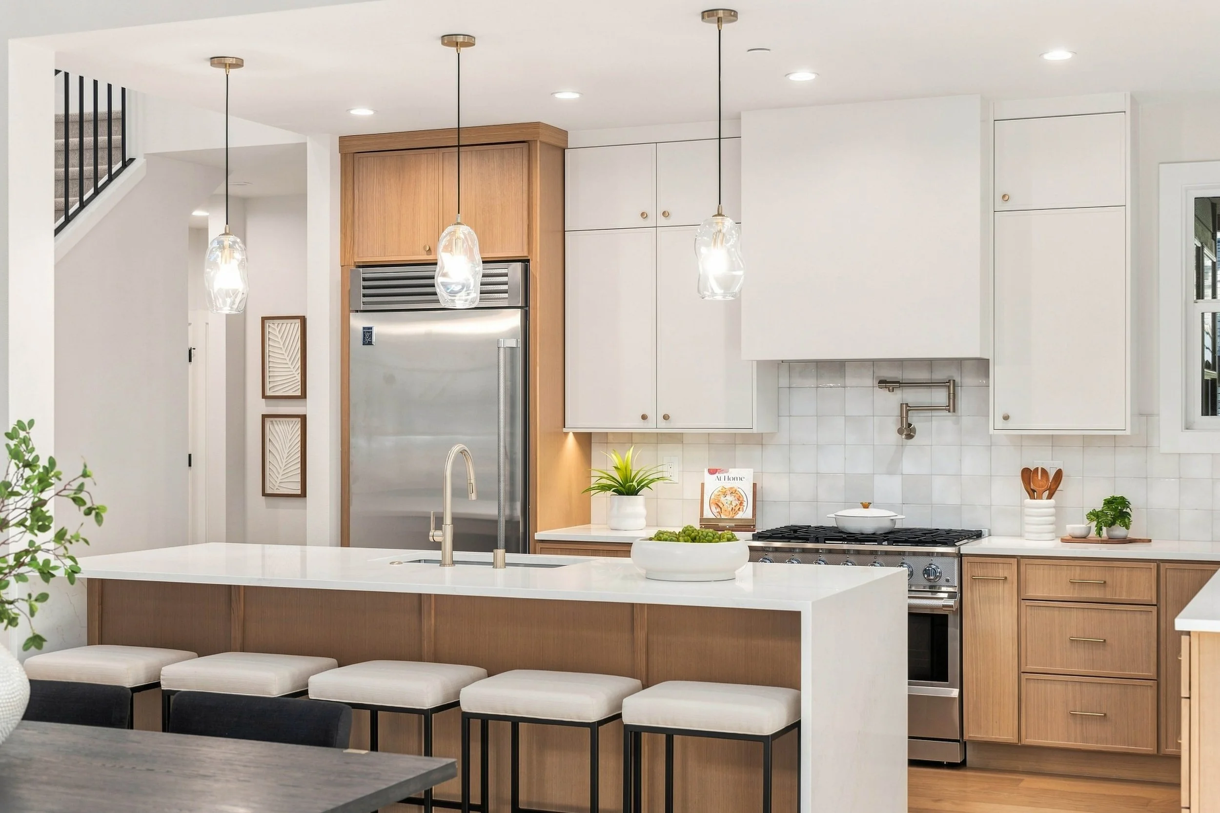 Modern kitchen with white countertops, light wood cabinets, a stainless steel refrigerator, and hanging pendant lights.