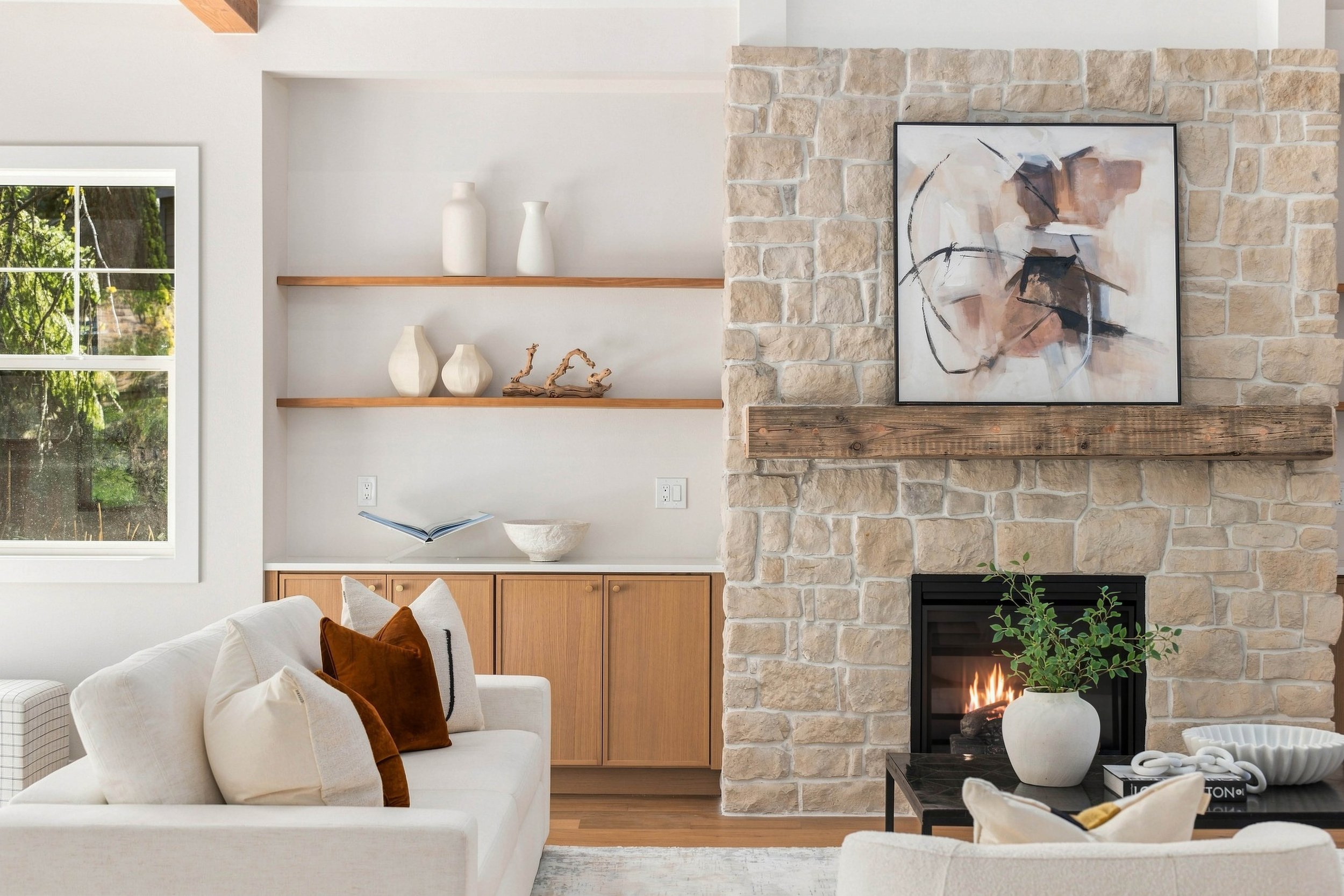 Living room with a stone fireplace, abstract art, books, vases, and comfortable seating.