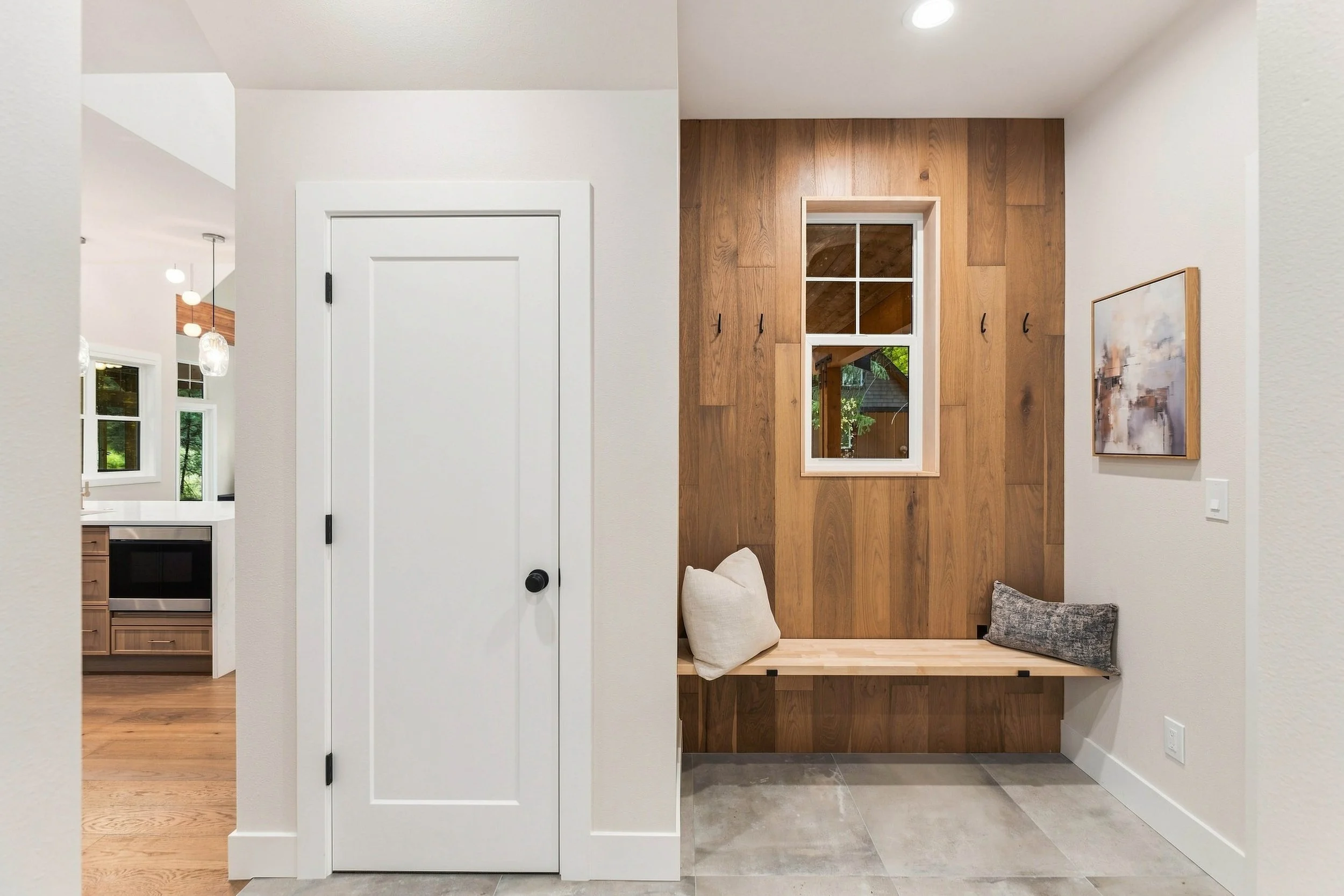 Interior view of a modern house with a white door, a wooden accent wall with a window, and a seating area with pillows.