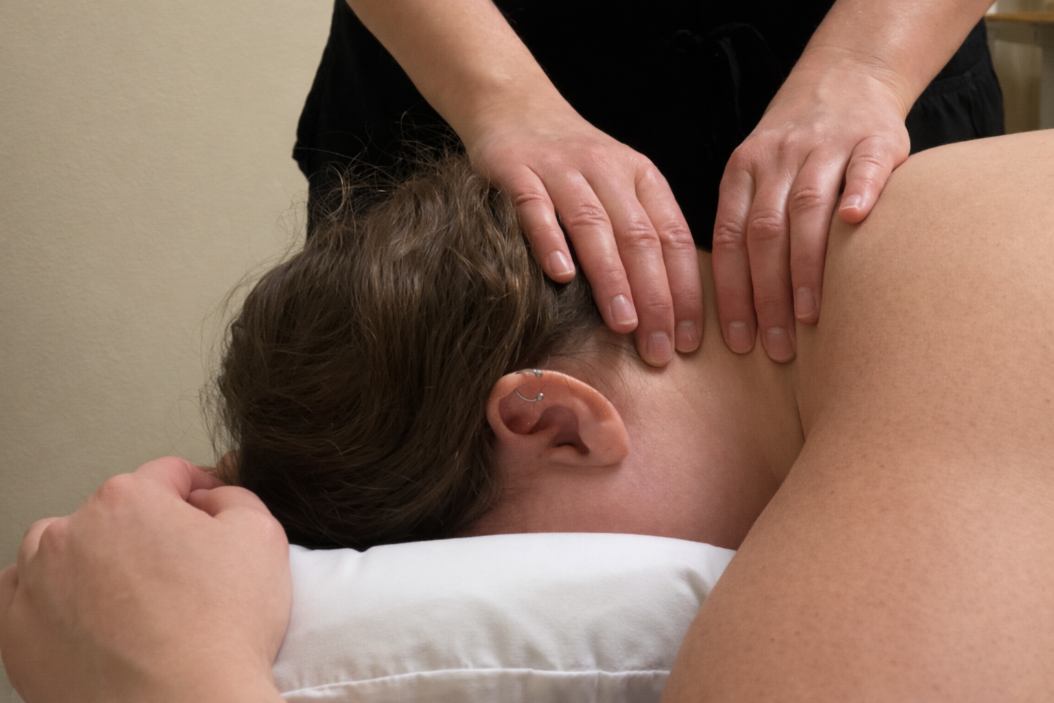 Person receiving a massage with hands placed on the neck and shoulder area.