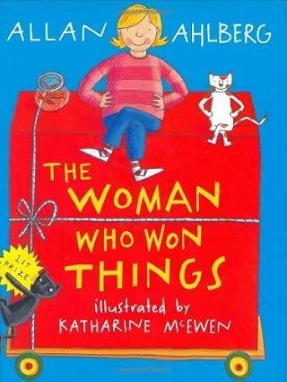 Cover of the book titled 'The Woman Who Won Things' by Allan Ahlberg, illustrated by Katharine McEwen, featuring a girl with blonde hair, wearing a red and pink striped shirt, sitting on a red box with a white cat, with a camera and a yellow sticker that says 'First Prize' nearby.