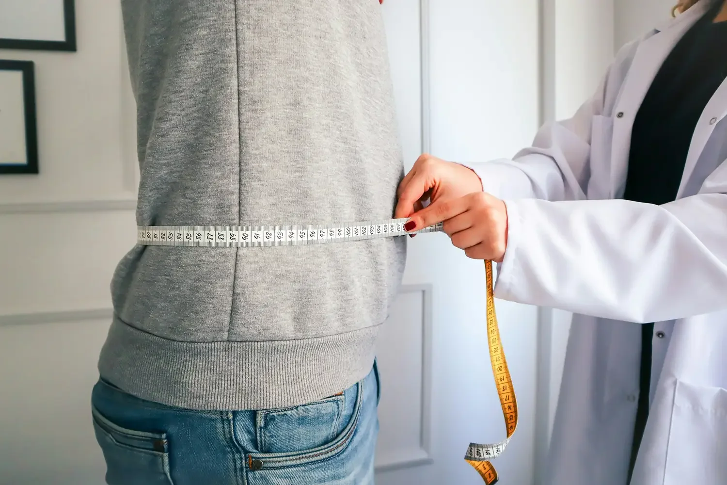 A medical professional measuring a patient's waistline with a tape measure to check metabolic health and obesity levels.