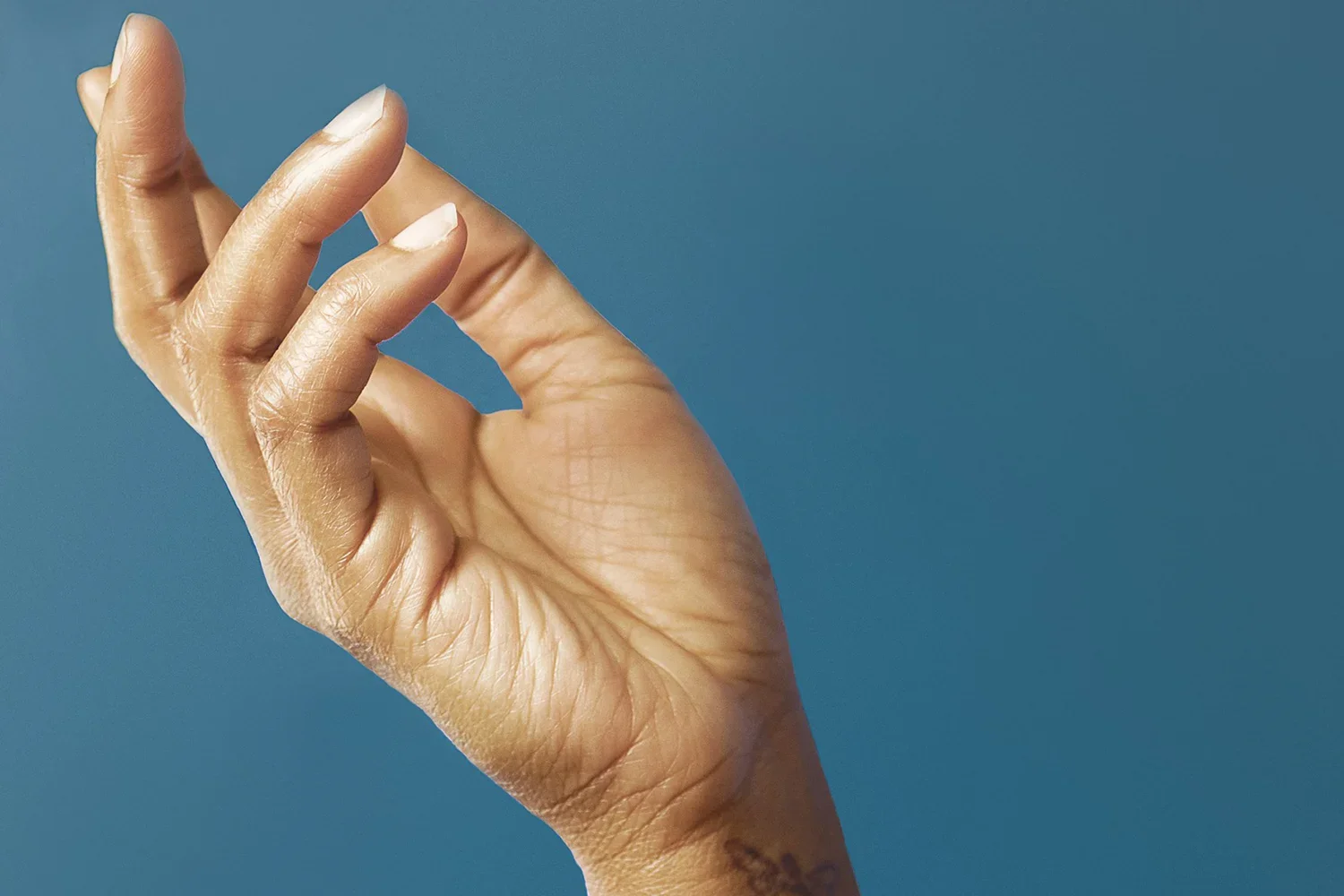 Close-up of a hand with natural, healthy nails against a blue background, illustrating the analog bio-marker concept for nail-based precision health signals.