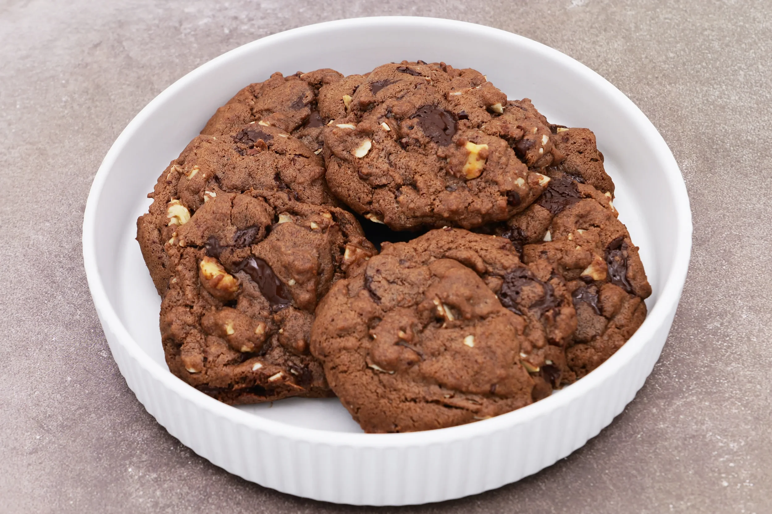 Gooey dark chocolate walnut protein cookies with melted chocolate chunks stacked on a white plate