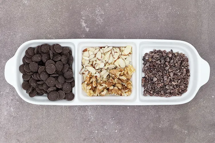 Dark chocolate wafers, chopped almonds and walnuts, and cacao nibs in a divided serving tray