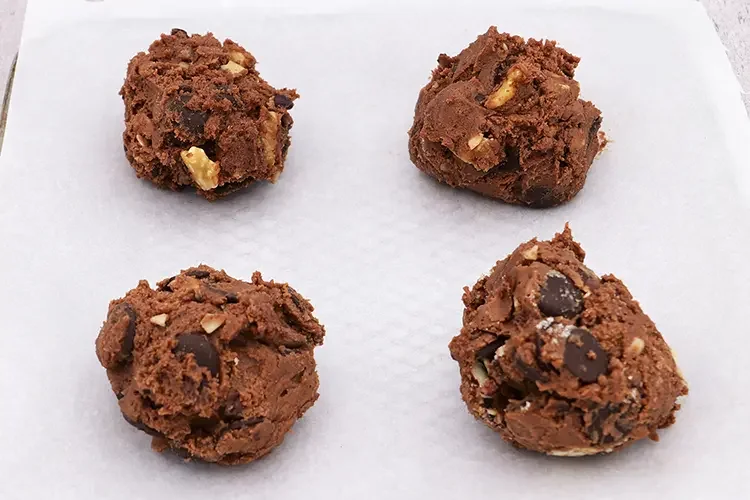 Four portioned cookie dough balls on a parchment-lined tray before baking