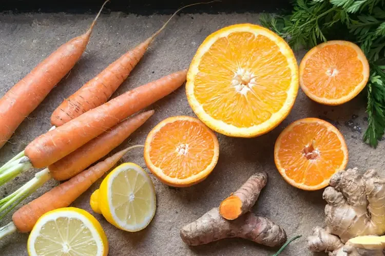 Fresh carrots, oranges, and ginger arranged to represent natural photo-protection and collagen-boosting nutrition.