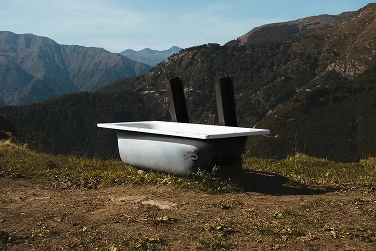 A white bathtub sitting in a vast mountain landscape under a clear blue sky, symbolizing a brain reset and somatic recovery through cold exposure.
