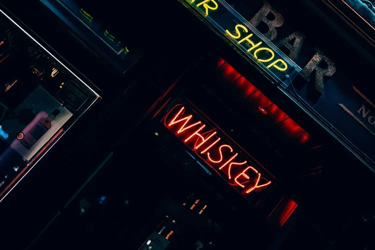 A vibrant night scene featuring glowing red "WHISKEY" and yellow "BAR SHOP" neon signs against a dark city background.