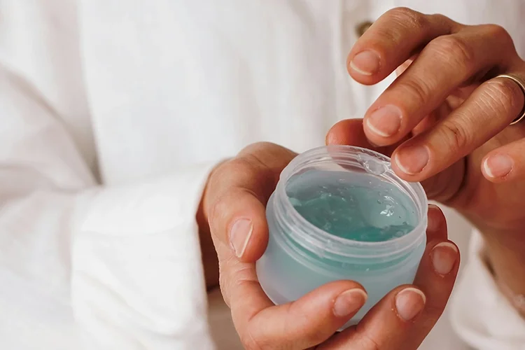 Close-up of hands holding an open jar of hydrating clear blue gel moisturizer.