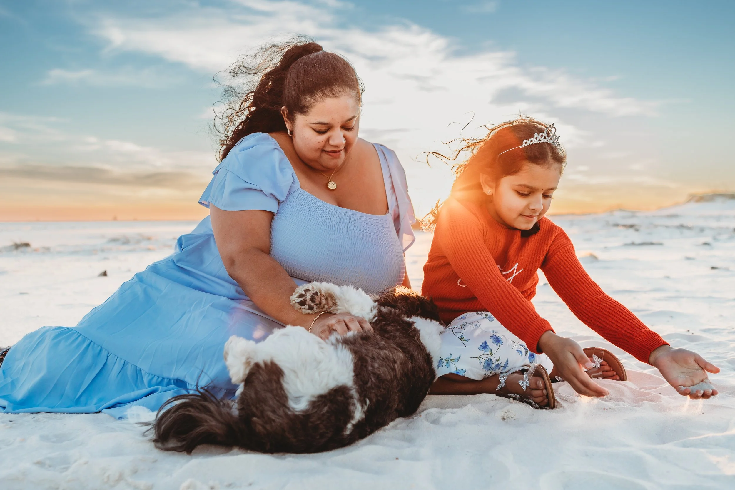 A mother, daughter and puppy playing in the sand on the beach at sunset in Fort Morgan beach in Alabama 
