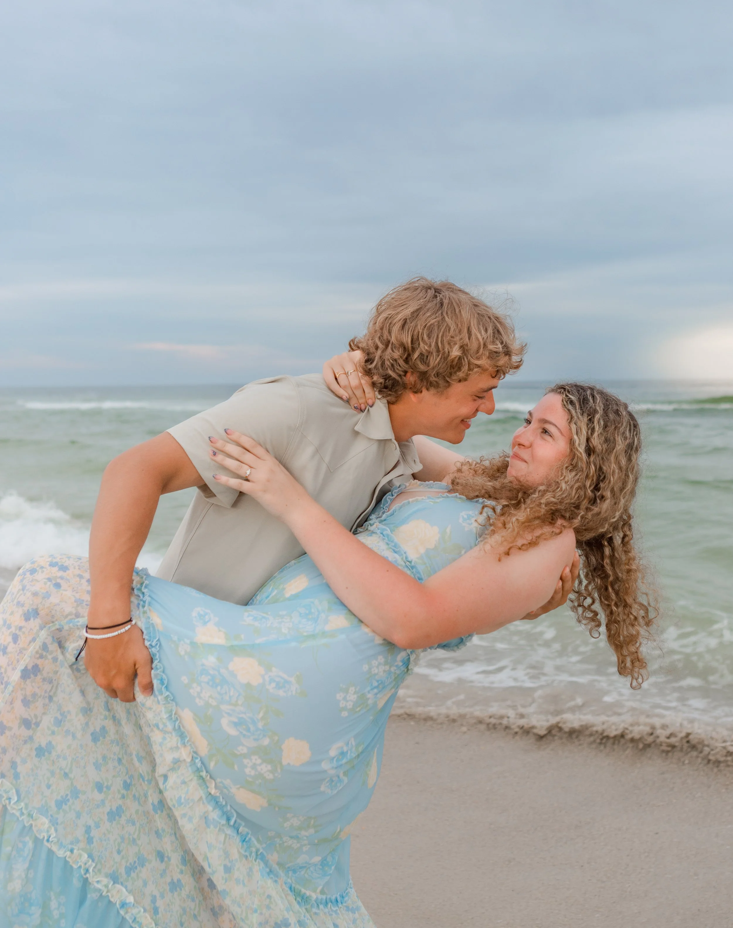 A close up of a young couple on the beach at sunset in Orange Beach, Alabama. They are close to the water and looking into each others eyes. 