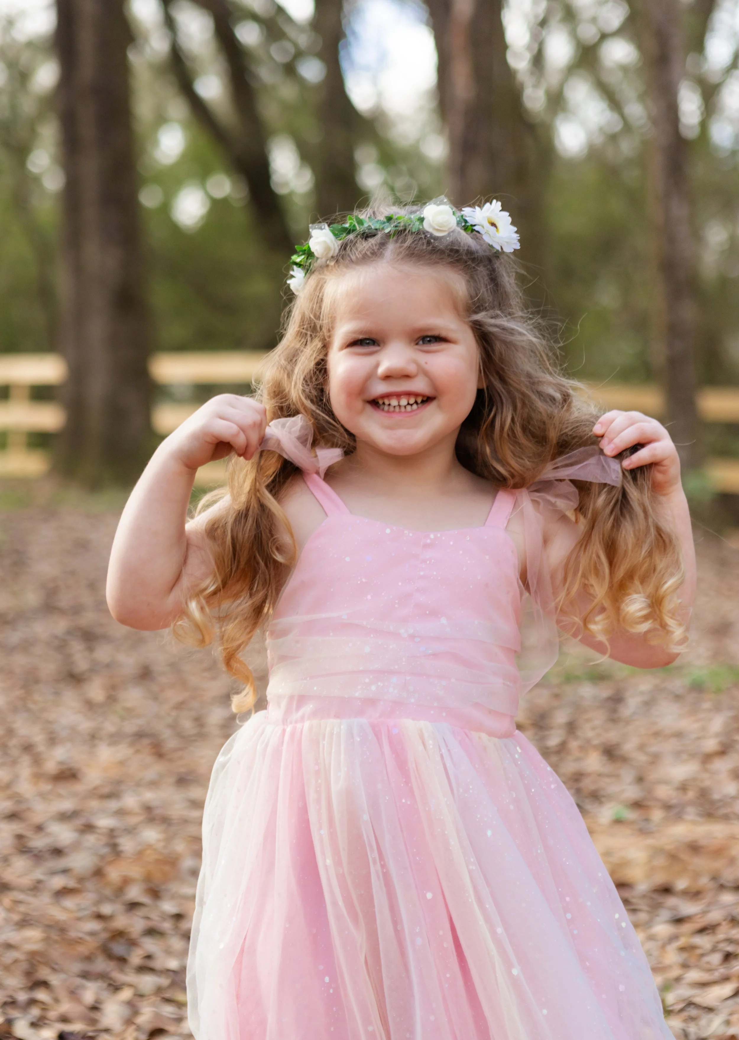 A beautiful little girl in a pink party dress with a floral crown with the biggest smile on her face
