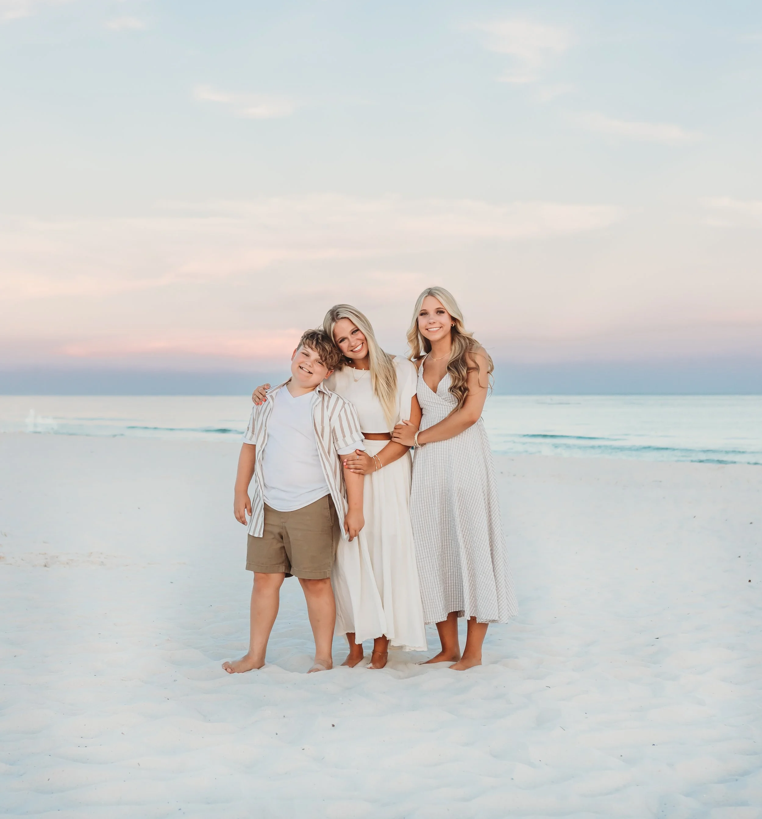 Group of three young adults standing on the beach at sunset.