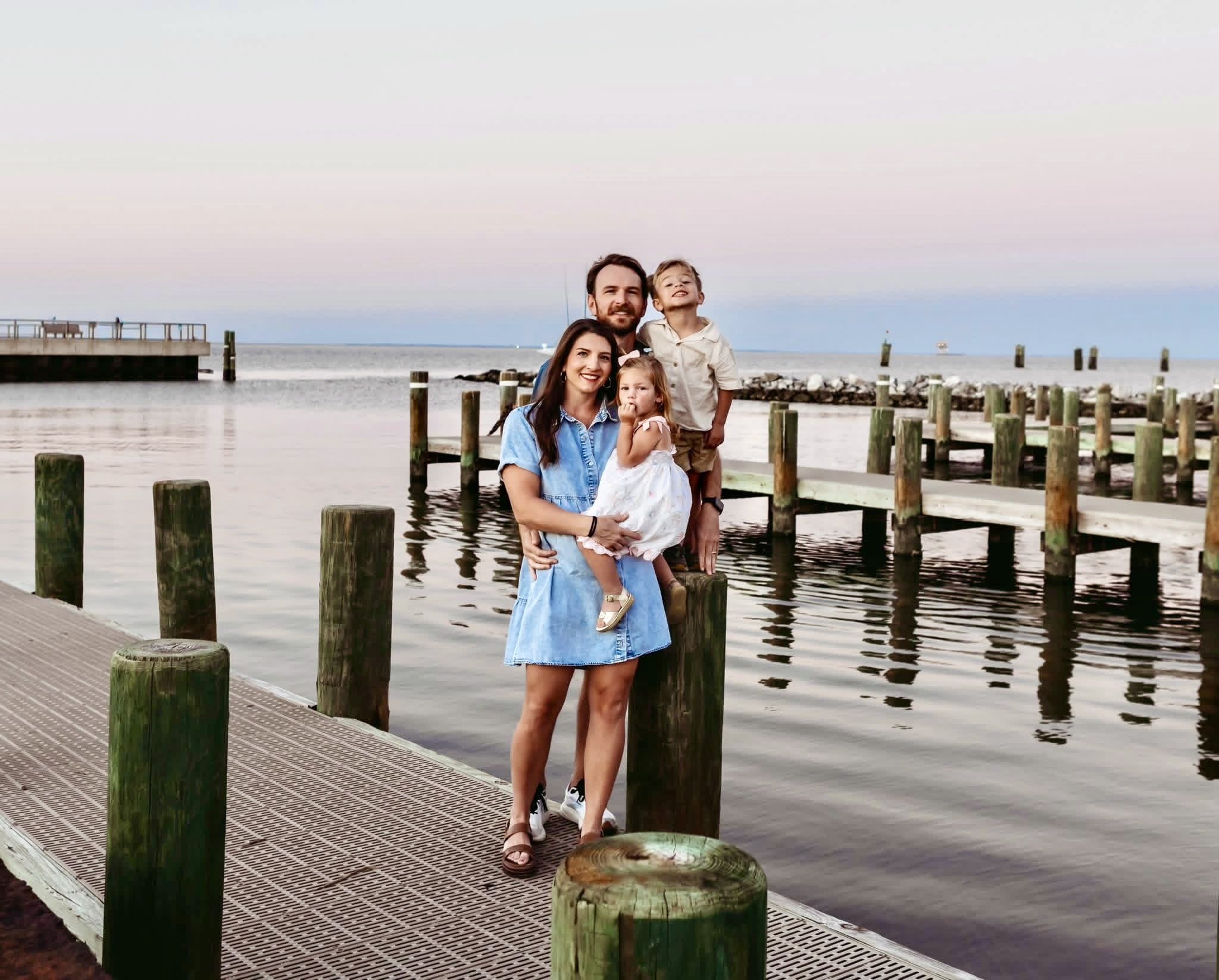 Family of four enjoying time on a dock by the water during sunset, smiling and posing for a photo.
