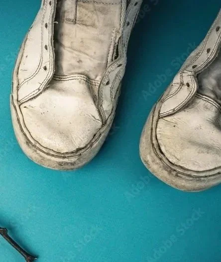 Close-up of worn white sneakers with scuffed soles on a blue surface.