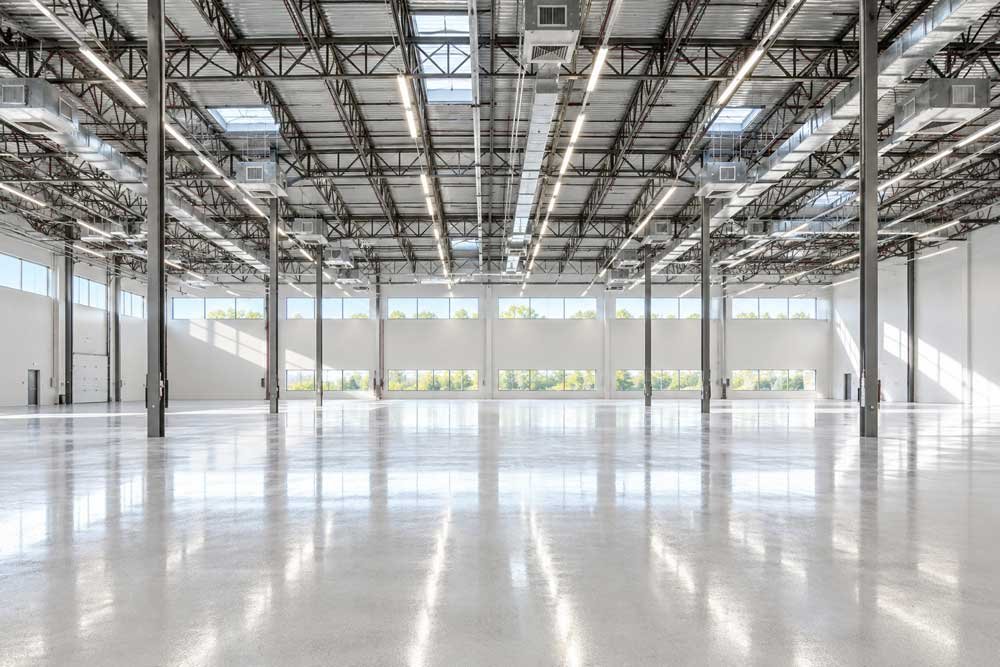 Empty industrial warehouse with high ceilings, metal beams, skylights, and large windows
