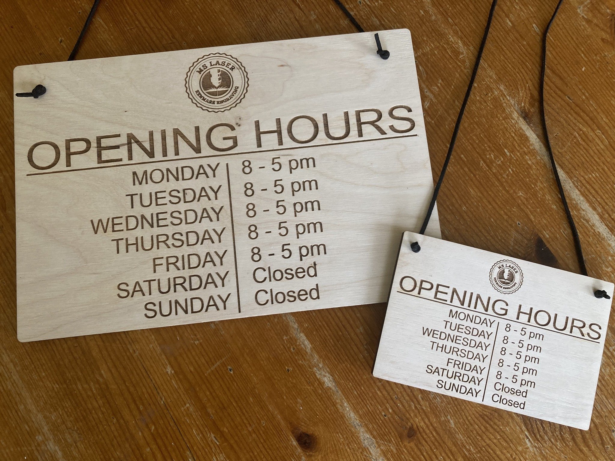 Two differend sizes signs showing the opening hours for a business. Engraved on plywood