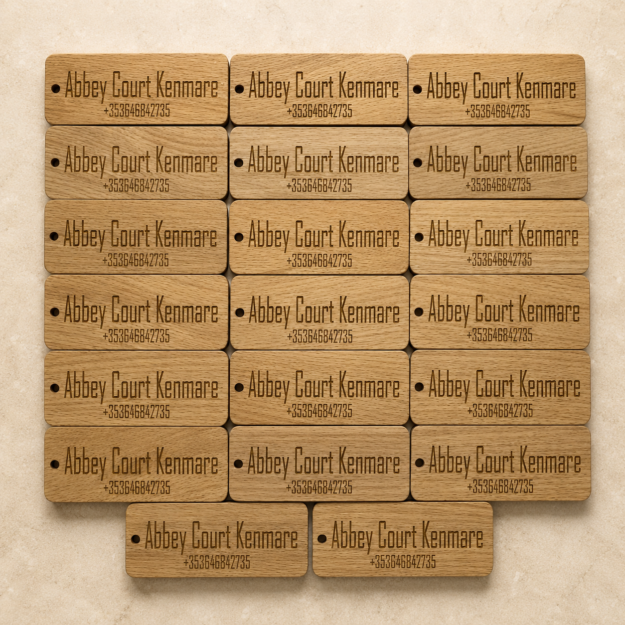 Collection of 15 wooden name tags engraved with 'Abbey Court Kenmare' and a phone number, arranged in a grid pattern on a beige background.