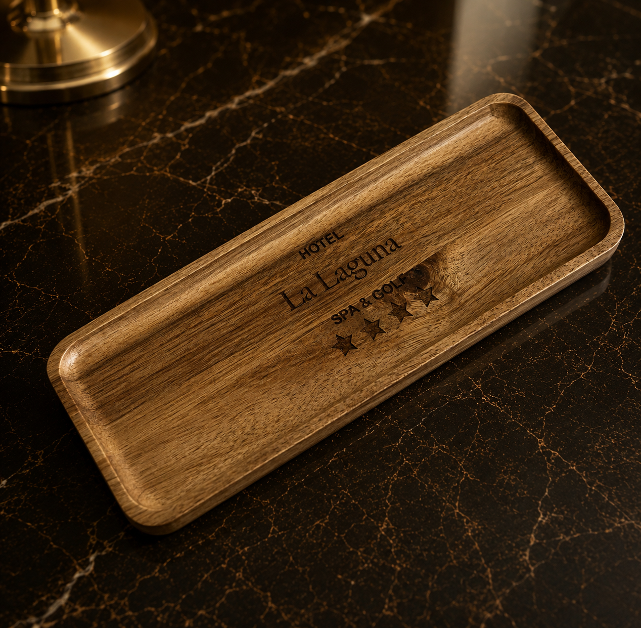 Wooden tray with engraved text reading 'Hotel La Laguna SPA & GOLF' and four stars below, placed on a dark marble surface.