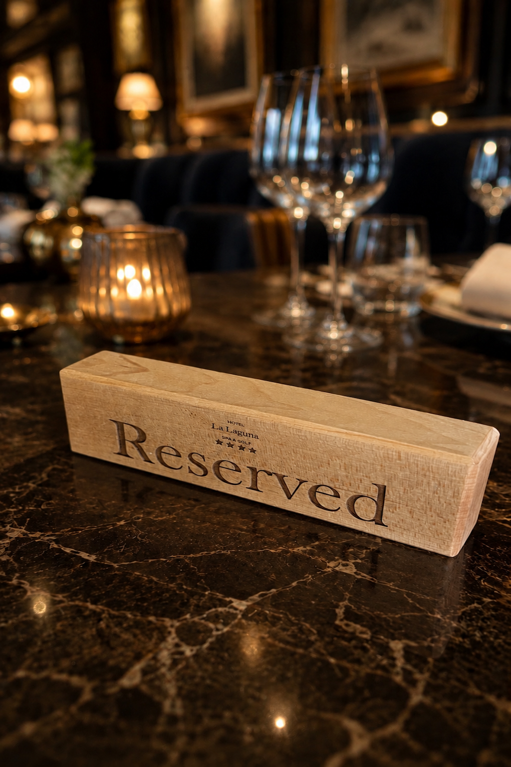 A wooden Reserved sign on a marble table at a restaurant, with wine glasses, candles, and dim lighting in the background.