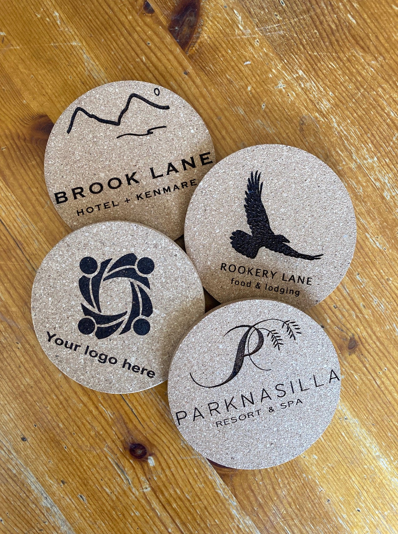 Four round cork coasters with different logos and text for various hotels and businesses.