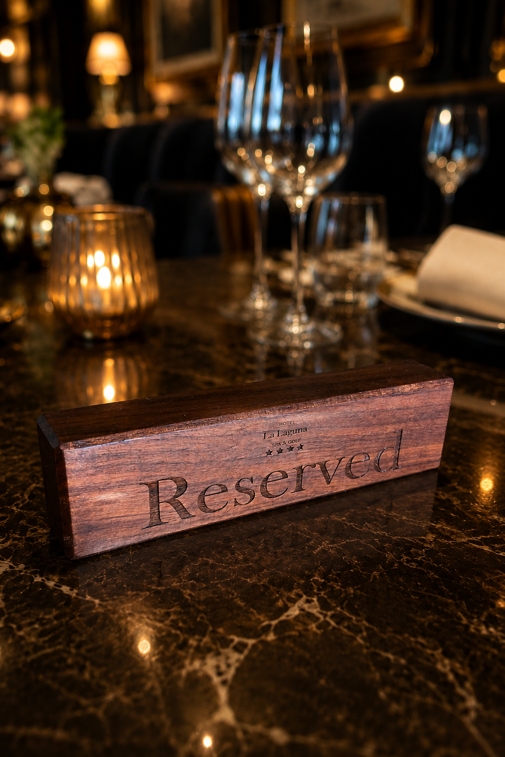 A wooden 'Reserved' sign on a dark marble table, with wine glasses, a napkin, and candlelit decor in the background.