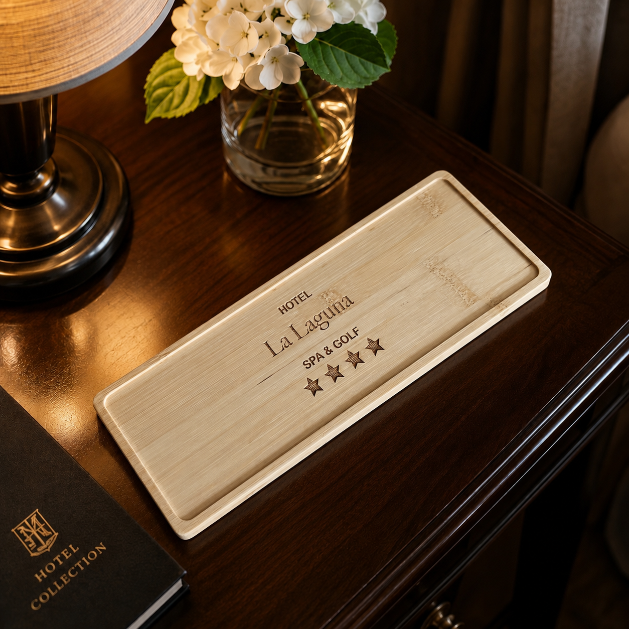 A hotel room desk with a wooden nameplate for La Laguna Spa & Golf, a lamp, a glass vase with white hydrangea flowers, and a hotel brochure.