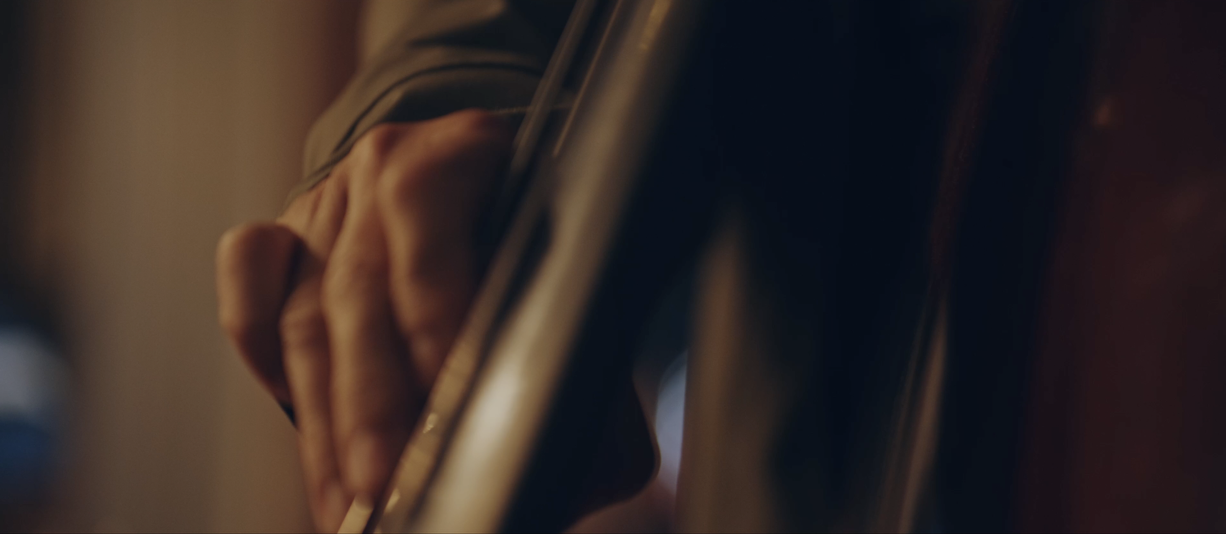 Nahaufnahme einer Hand, die auf die Seite eines Musikinstruments, wahrscheinlich eines Violins, greift.