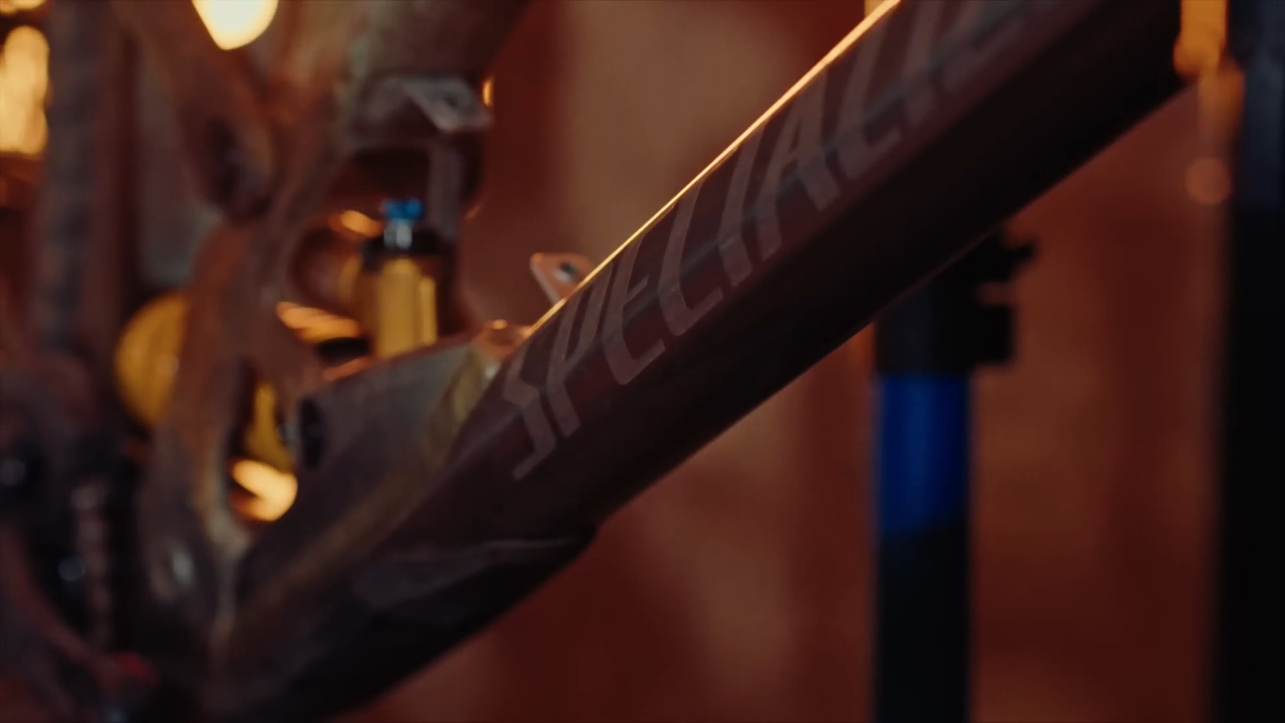 Nahaufnahme des Rahmenrohrs eines Fahrrads mit dem Logo "CERVELO" im Fokus, im Hintergrund eine Fahrradgabel und unscharfe braune und blaue Elemente.