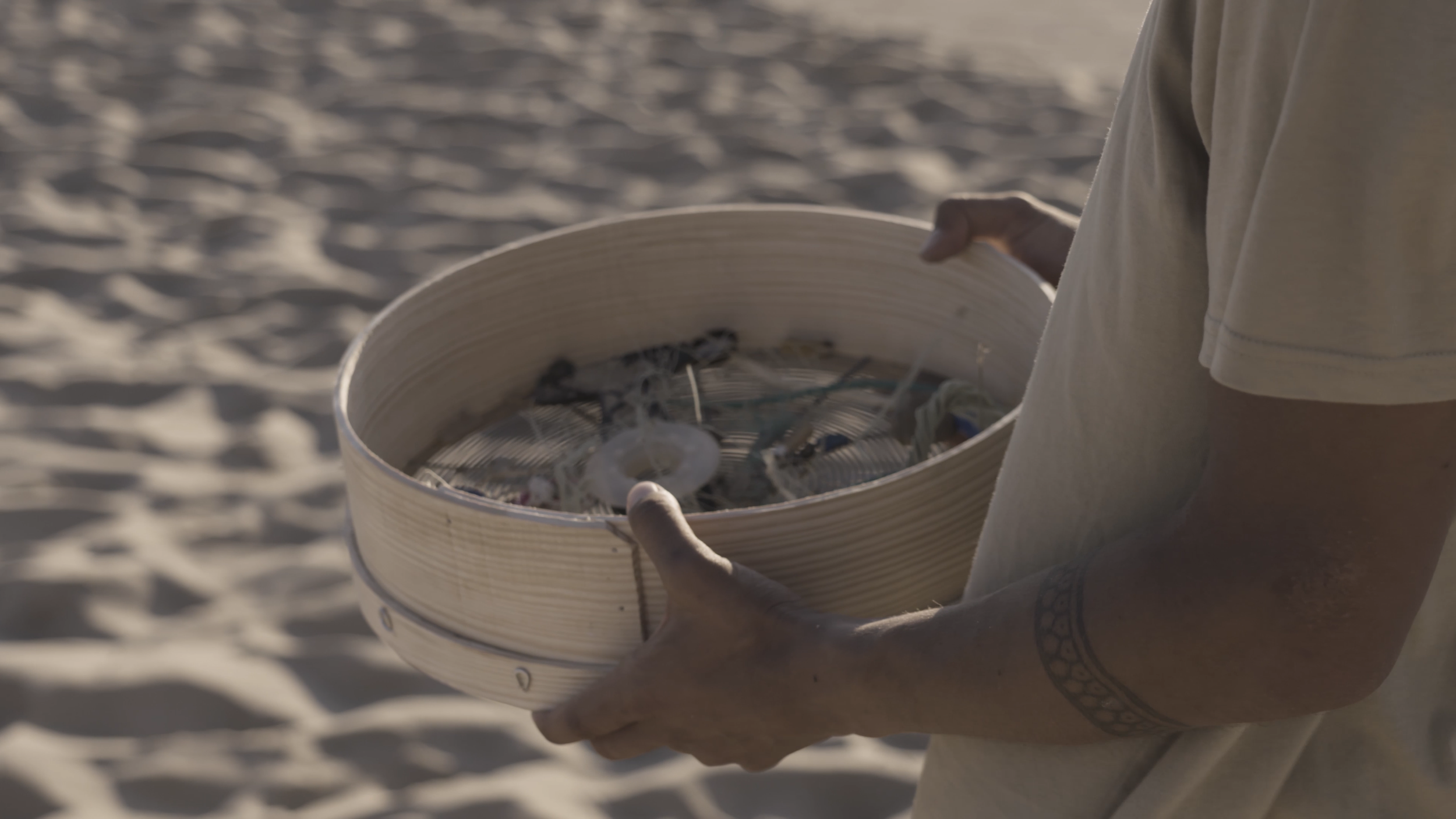Eine Person hält einen Korb mit Muscheln und Meeresfundstücken an einem Sandstrand.