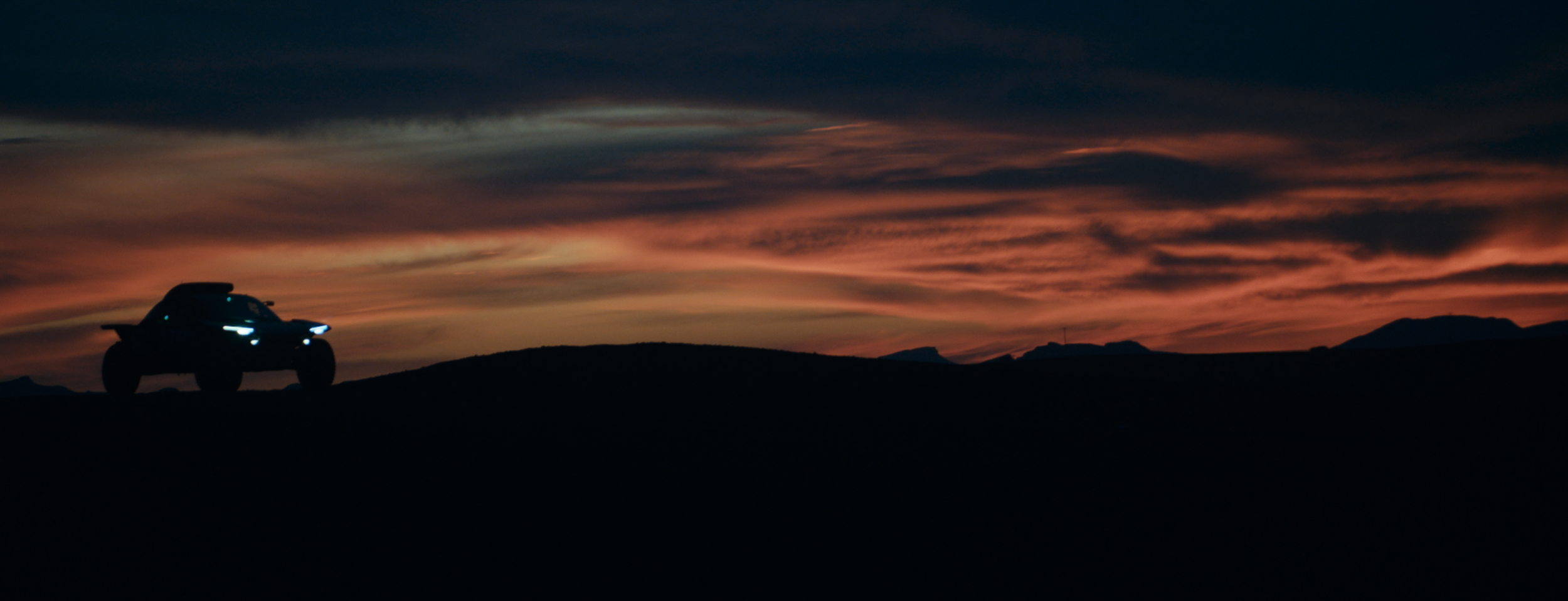 Silhouette eines Autos auf einem Hügel bei Sonnenuntergang mit einem bunten Himmel.