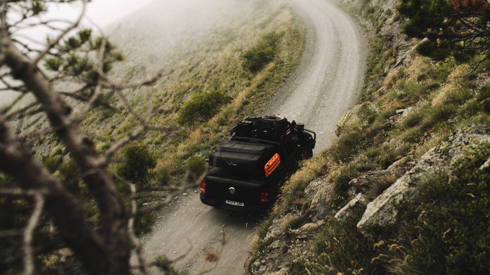 Ein Off-Road-Fahrzeug fährt auf einer schmalen, kurvigen Bergrückstraße durch neblige, bergige Landschaft.