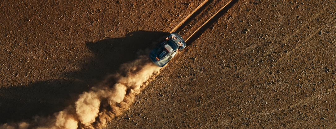 Ein Hochgeschwindigkeitsauto mit Audi-Logo fährt über staubige Strecke und wirbelt Staub auf.