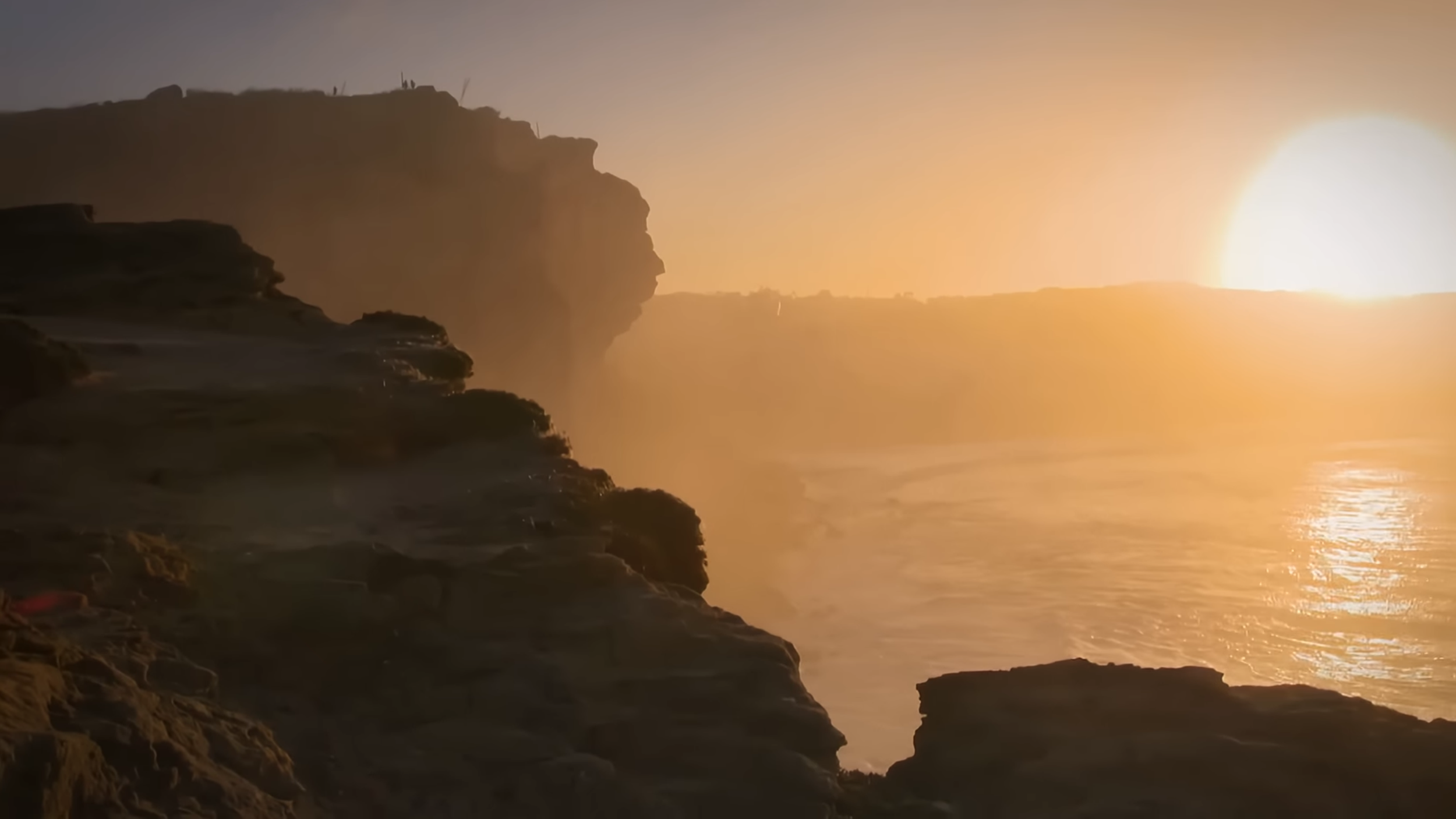 Sonnenuntergang über den Klippen des Meeres mit Wellen, die gegen die Felsen schlagen.