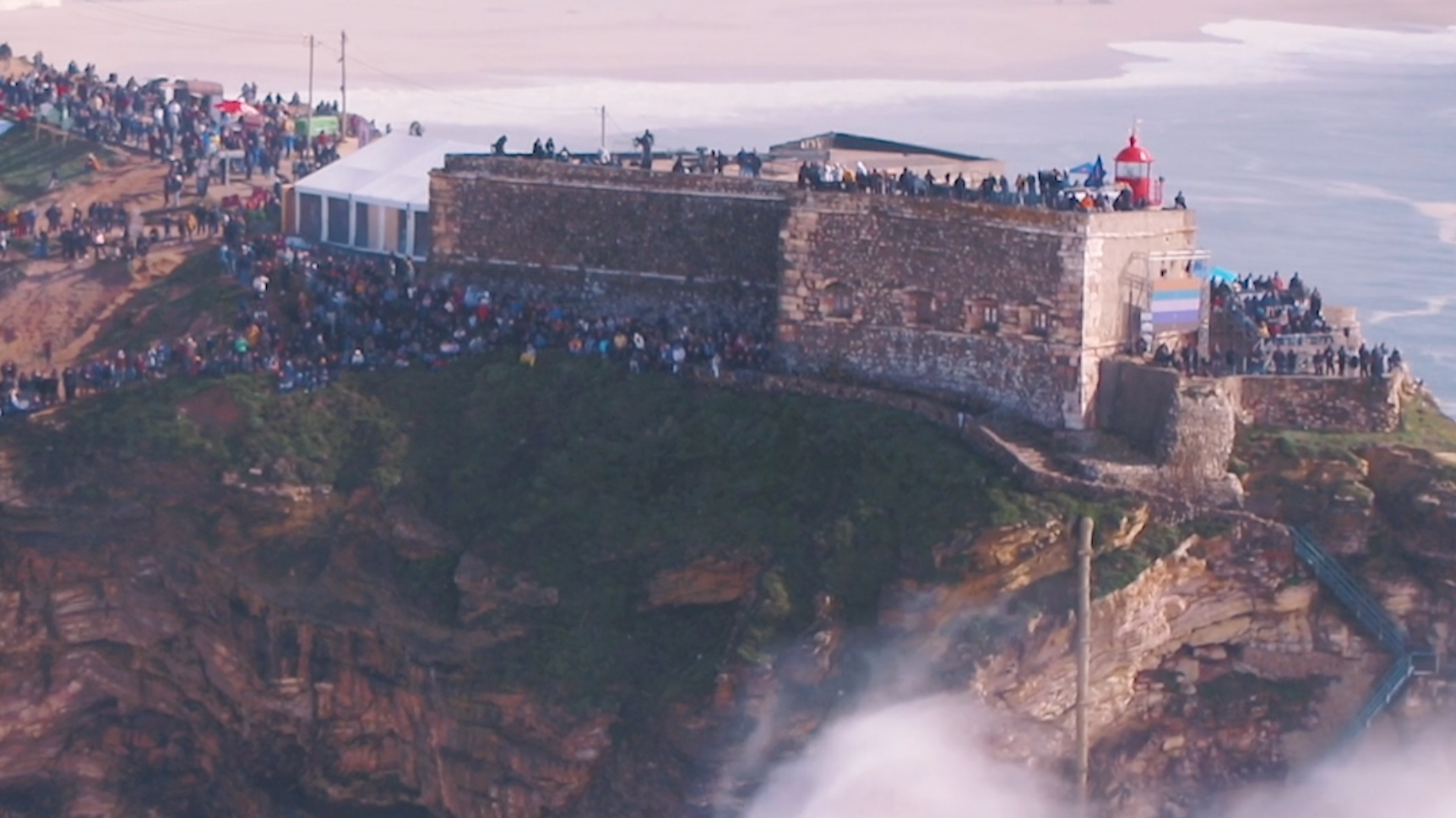 Der Leuchtturm auf dem Felsen neben dem Meer, umgeben von einer großen Menschenmenge auf der Festung, bei Sonnenuntergang.