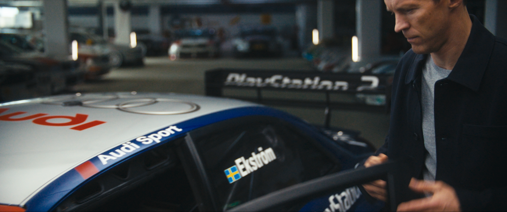 Ein Mann steht neben einem Audi-Rennwagen mit den Labels "Audi Sport" und "Ekstian" bei einem Rennen oder einer Rennstrecke.