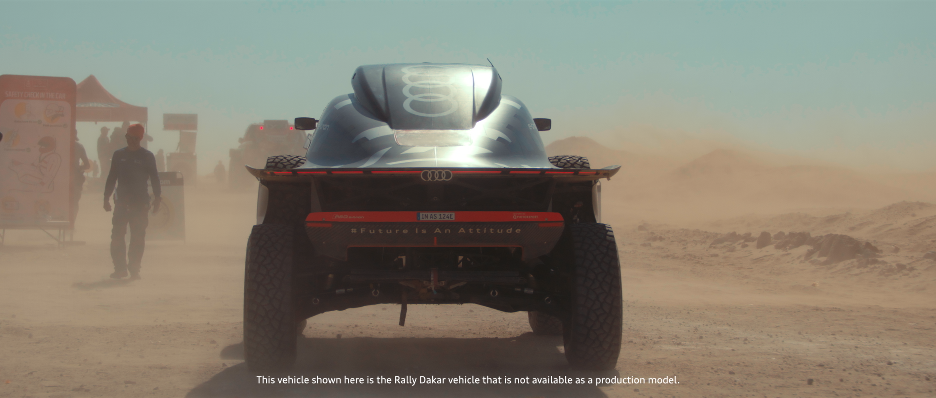 Rally Dakar Fahrzeug auf staubiger Wüstenstraße, im Hintergrund Zelte und Menschen.